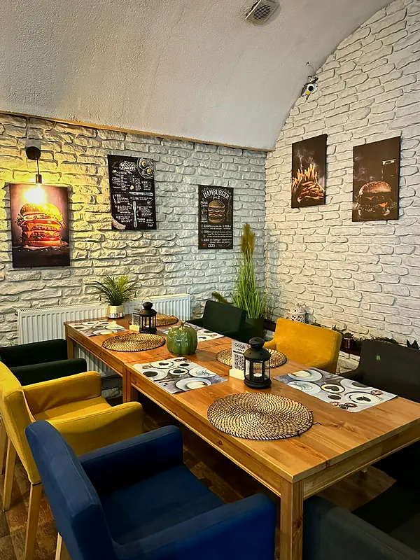Stół z kolorowymi fotelami pod ceglaną ścianą z grafikami