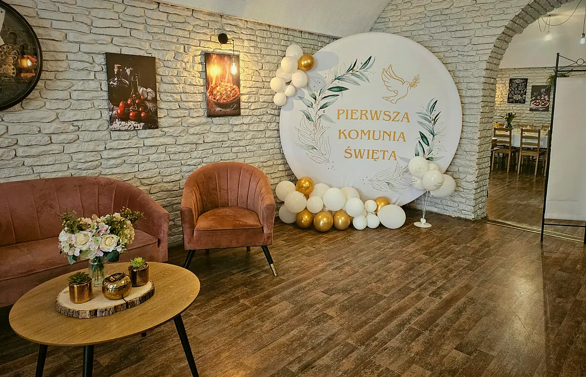 Ścianka komunijna z balonami obok kącika z różową sofą i fotelem